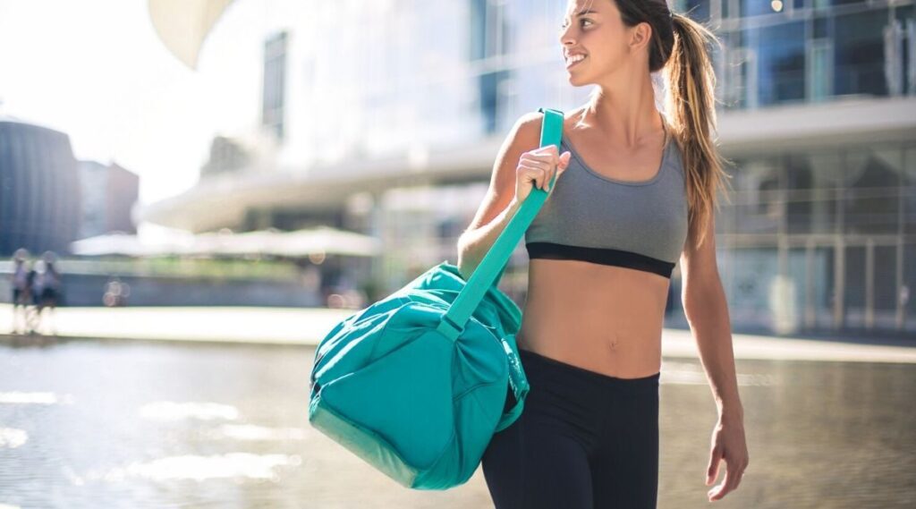 a girl walking on a road holding a gym bag on her shoulder