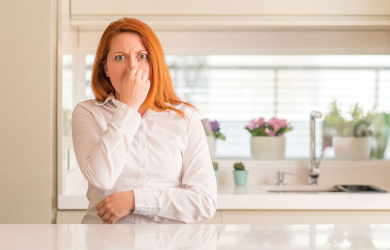 a woman in kitchen smelling something as she has hand on her nose