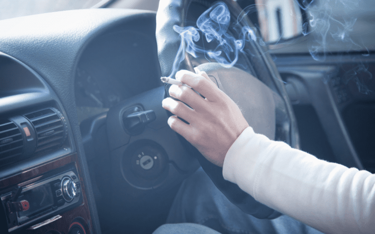 close shot of car steering wheel and a cigarette in a hand.