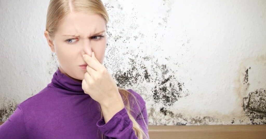 a picture of a woman feeling smell and hand on her nose and mold on wall in background