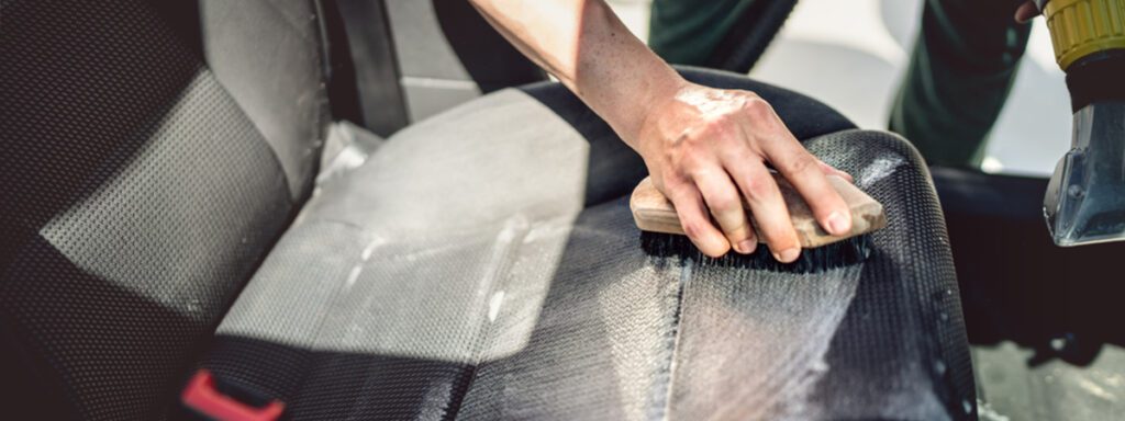 close shot of a hand with brush cleaning car seat.