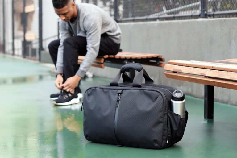 a gym bag in picture and a man is siting in locker room tying laces in background