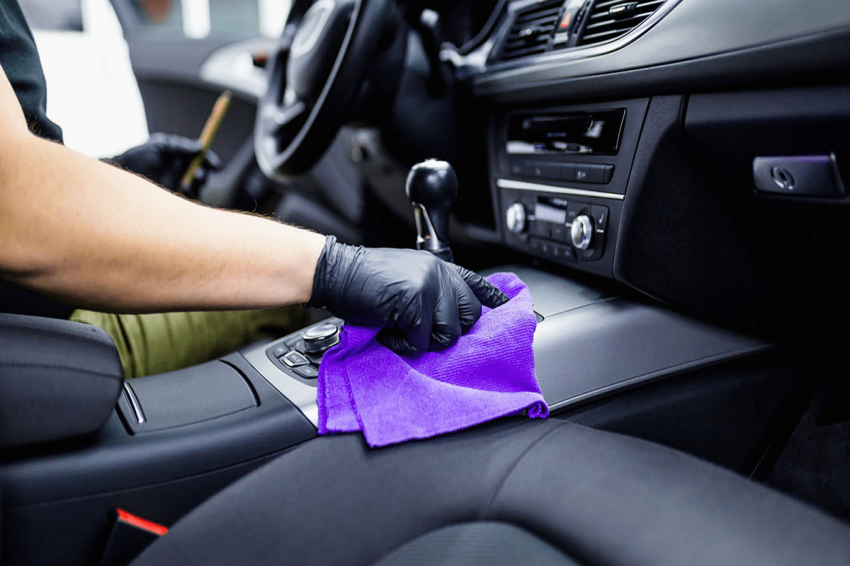 close shot of hand cleaning car interior with purple color cloth.