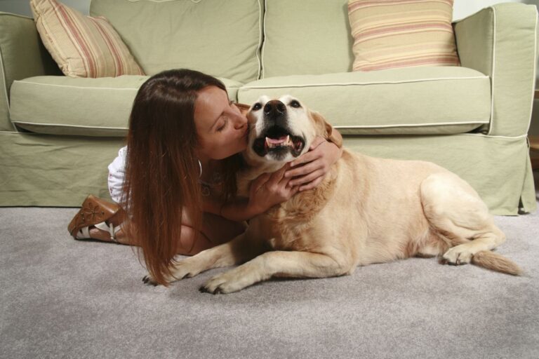 a woman sitting on carpet, hugging and kissing her dog.